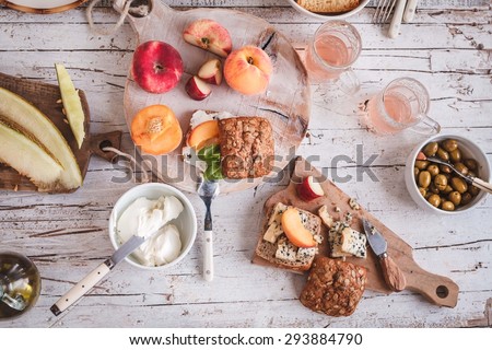 Summer lunch served on a white wooden picnic table with fruits, various cheese, olives and fruits juice  from above. Rustic mediterranean atmosphere outdoors.