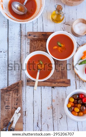 A Delicious cold gazpacho soup in white bowl with bowl tomatoes cherry and bottle of olive oil over on a rustic white wooden kitchen table from above. Traditional spanish cold soup. Step on step.