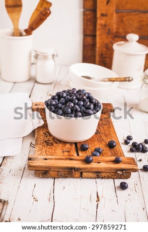 A ceramic bowl served with fresh blueberry over on a  vintage wooden table in white shabby chic background with white crockery. Rustic white styling.