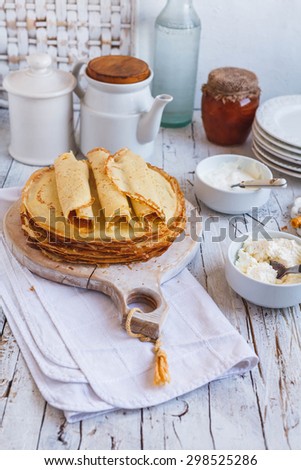 A crepes folded in rolled form served on rustic cutting board with rustic kitchen cookware on white wooden table. Rustic styling image. Homemade food concept.