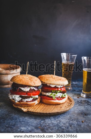 Fresh homemade two veggies burger served on round rustic cutting board over on blue rustic table with two glasses of beer. Rustic dark styling.