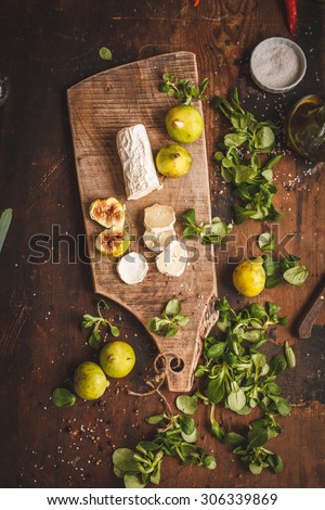 Meat gourmet snack. Goat cheese and green fig and  salad herbs on rustic wooden board over dark grunge backdrop, top view