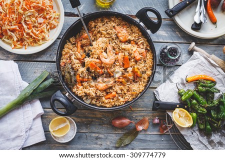 Traditional spanish real food. Homemade prepared paella with chicken meat and seafood produce in pan from above on wooden table with different bbq veggies. Rustic style.