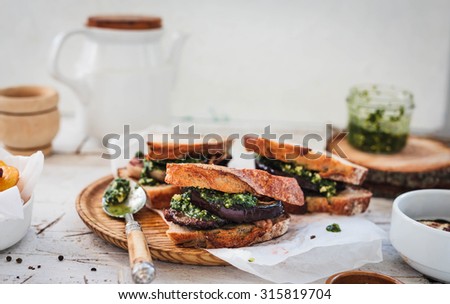A making perfectly whole sandwiches with bbq veggies, roasted beef fillet steak and sauce pesto over on a round rustic cutting board with sauce pesto. House made sandwich concept