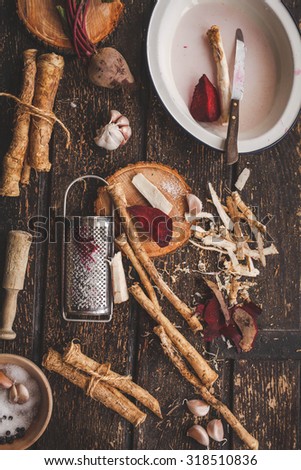 A lots of horseradish root and beetroot with knife over on a cutting board on a old wooden table. Horseradish and beet roots for food which is a root of plant. Rustic dark style.