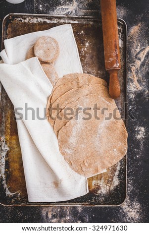Rolled wholegrain dough with dough balls and rolling pin over on a flourish baking dirty sheet on a  dark table. Step on step preparing flatbread.