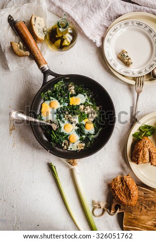 Ideal idea for breakfast meal. A cast-iron pan of fried Quail eggs and spinach veggies with leeks over on a vintage linen napkin. Rustic style.