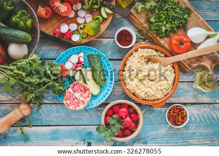 Various fresh vegetables on a blue wooden table  and cook burghul in ceramic bowl ready to prepare arabian traditional food. Country food concept from above. Series.