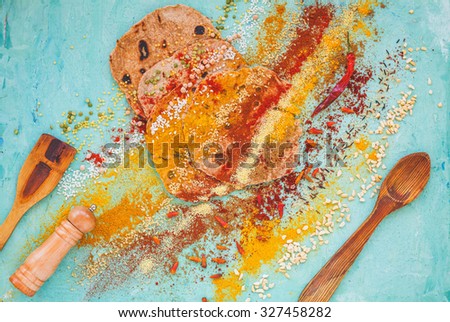 Abstract composition over on wholegrain flatbread with spices and bio cereals products scattered over on azure background with vintage spoon. Rustic style. Healthy, real simple food concept