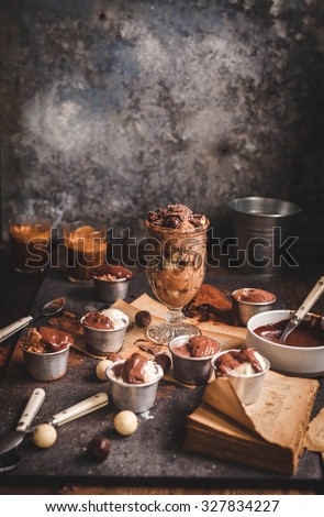 Still life with chocolate coffee ice cream balls in jars on a vintage grey table with chocolate cream and cappuccino glass. Vertical rustic dark image.