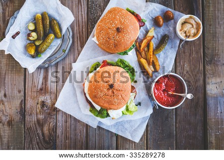 Fresh homemade two  burgers on dark serving board with spicy tomato sauce, vegetables  and marinated cucumber over dark wooden background. Top view