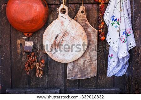 Home country kitchen farmstead concept. Old cutting board, linen embroidery, ceramic pan and dry peppers hanging on a grunge vintage wooden wall. rustic dark style