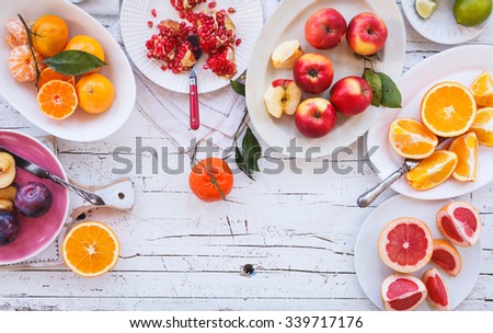 Colorful festive assortment of purple, red and orange fruit background in bowls. Lime, pomegranate, tangerine, orange, mandarin, apple, plum, grapefruit, lime sliced above white rustic tabletop.