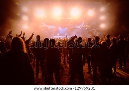a crowd of young people at the concert, their silhouettes illuminated by powerful lights