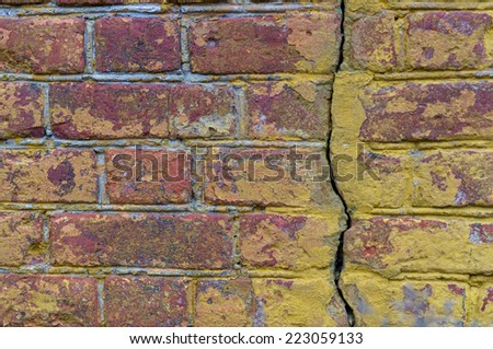 a ragged red and yellow painted brick wall with big split through the bricks