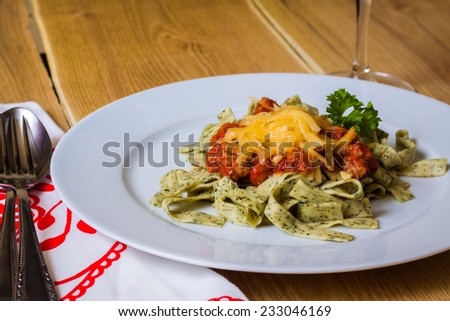 Delicious green herb pasta with bolognese sauce on white plate with fork and spoon, wooden background