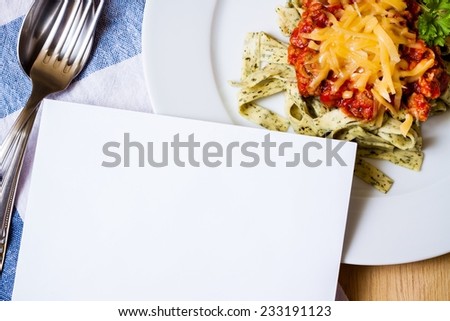 Blank card with delicious green herb pasta and bolognese sauce on white plate with fork, spoon and dishtowels