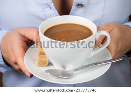 Hand holds mug of coffee with milk with spoon and brown sugar