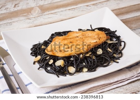 Roasted chicken with black spaghetti, maple syrup and almonds on a wooden desk