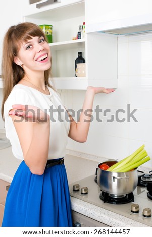 Young cheerful female standing in front of stove with her hands raised. The saucepan full of raw vegetables. The soup is not getting cooked.