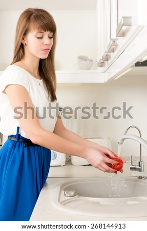 Young female washing tomatoes under tap water on the kitchen