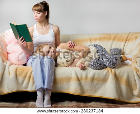 Young female reads a book for her sister while she is lying on t