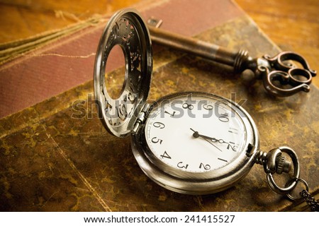 Vintage grunge still life with hour glass, pocket watch, old brass keys and tattered book.