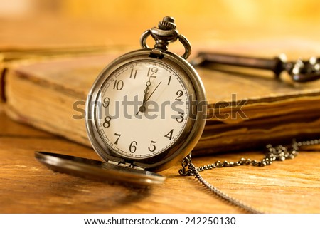 Vintage pocket watch on wooden surface against old book