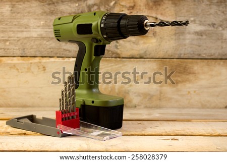 Drill and set of drill bits over wooden background