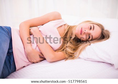Beautiful young woman sitting on bed and suffering from abdominal pain