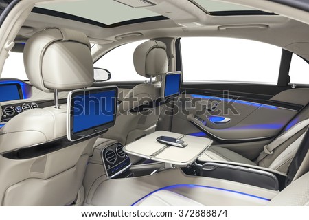 Car inside. Interior of prestige modern car. Back seats with displays, tables & mobile phone. White cockpit with panoramic roof & blue ambient light on isolated white background.