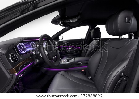 Car inside driver seat. Interior of prestige modern car. Front seat with display,steering wheel & dashboard. Black cockpit wood & metal decoration & violet ambient light on isolated white background.