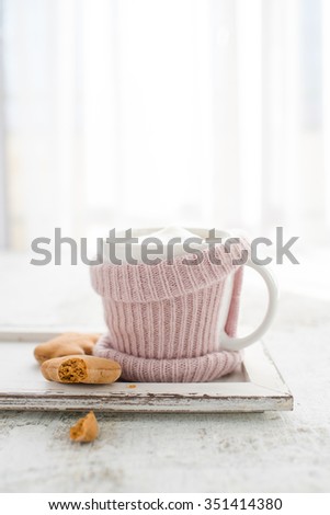 Cup of hot drink and gignerbread. Winter concept. Mug in pink knitted mitten standing on a white vintage white tray on white background