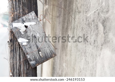 dirty wooden board sign on wooden post near concrete wall