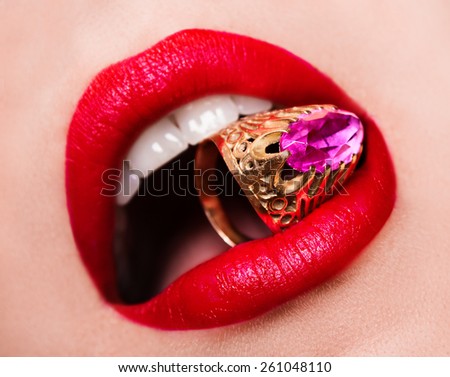 Close-up of beautiful woman\'s lips with bright fashion dark red glossy makeup. Macro lipgloss cherry make-up. Mouth with wedding gold diamond ring. Jewelry accessories.