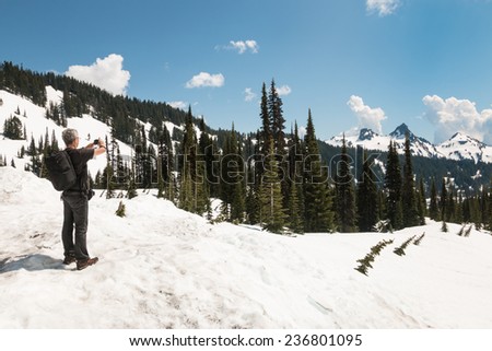 Man in summer clothes stand on snow and takes pictures of mountain peaks