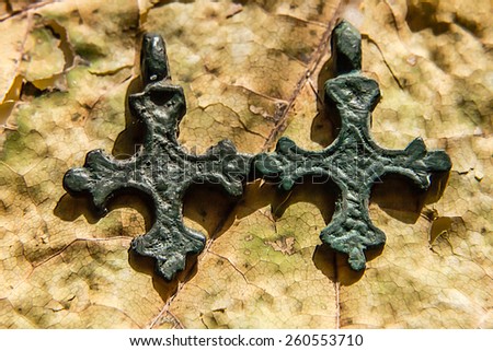 two medieval copper Christian crosses in a strong patina against dry leaves
