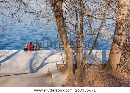 three young people have a rest on the river bank in the early spring