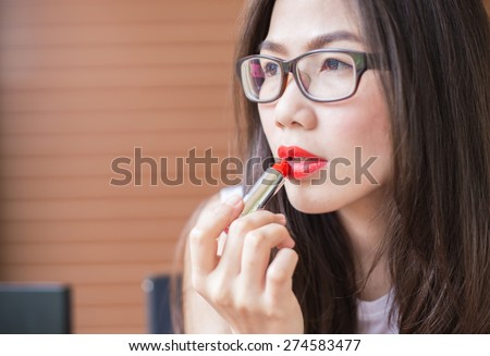 Beautiful Asia woman with perfect skin paints her lips red lipstick