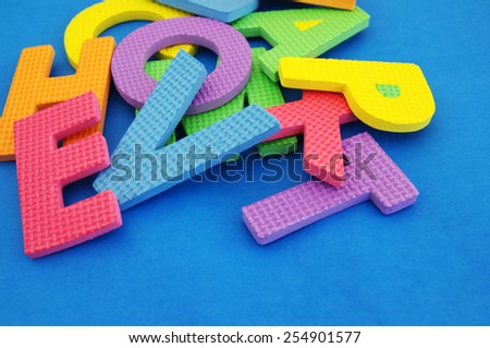 Color letters of the alphabet are chaotically scattered on blue paper / Bright different color of a letter of the alphabet