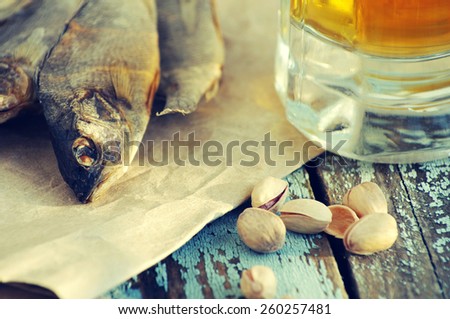 Beer in a glass, salty fish and pistachios on a textural wooden table. Beer and beer snack.
