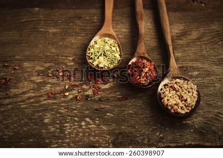 Three brown wooden spoons with spices for food on an empty impressive brown wooden background/ Spices in wooden spoons