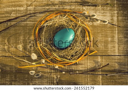 Easter egg in a nest with bright tapes with willow branches on a wooden background. Easter card.