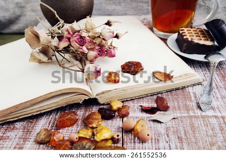 Dry roses, amber and the empty open book on a wooden textural table