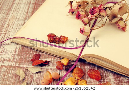 Dry roses, amber and the empty open book on a wooden textural table