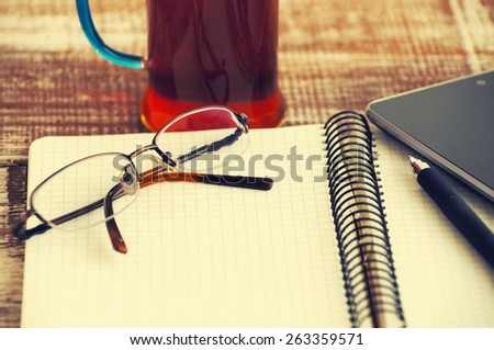 Points, open notebook, the tablet, the handle and cup of tea on a textural wooden table.