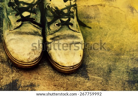 Old dirty boots with the untied laces on grunge a background. Old footwear.