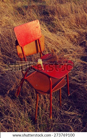 Two old chairs and bouquet from dry flowers and herbs in a dry grass in the open air in evening beams of the sun. Old furniture