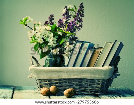Books and spring flowers of a lilac in a wattled basket on a wooden surface. A vintage still life with books and flowers