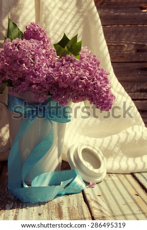 Lilac flowers bouquet in the jug decorated with a blue bow in vintage style. Vintage Bouquet of lilac flowers